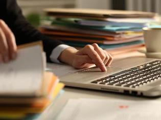 A person sitting in front of a computer and a stack of documents.